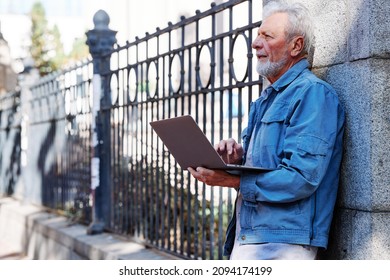 A Senior Student Stands In Front Of His University With A Laptop In His Hands And Checking On Test Results. Seniors In Retraining.