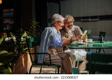 A senior stylish couple is sitting in an outdoors cafe using their smartphone. - Powered by Shutterstock