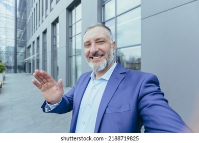 Senior Successful And Experienced Gray Haired Man Looking Into Phone Camera And Smiling Talking On Video Call, Businessman Taking Selfie While Standing Outside Office Building