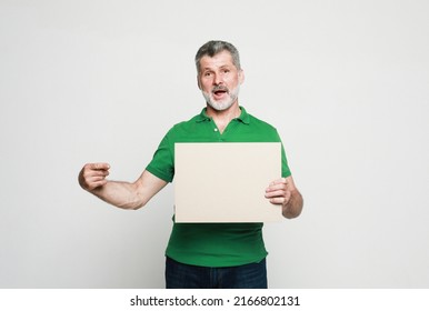 Senior Surprised Man With Mustache And Beard Holds The White Sign In A Studio Over Light Grey Background. Look Here, Great Offer.