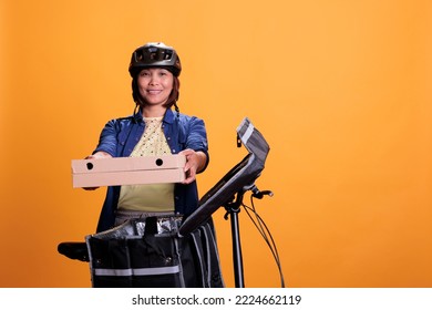 Senior Take Away Delivery Employee Delivering Takeout Food In Cardboard Box To Client, Using Bike As Work Transportation. Restaurant Worker Wearing Blue T Shirt And Cap While Working As Courier