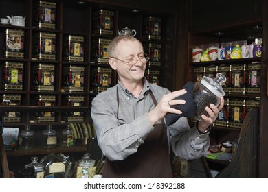 Senior Tea Shop Owner Dusting Jar Of Tea