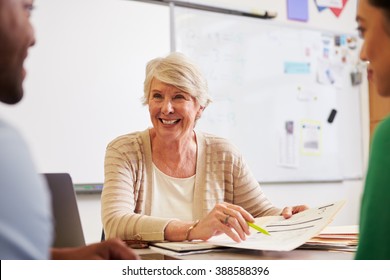 Senior Teacher At Desk Talking To Adult Education Students