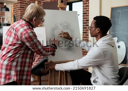 Senior teacher explaining sketching technique to african american student during art lesson in creativity studio. Artist man drawing vase model on canvas learning new sketch skill for personal grow