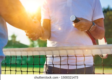 Senior tennis player shaking hands in court with yellow lens flare in background - Powered by Shutterstock