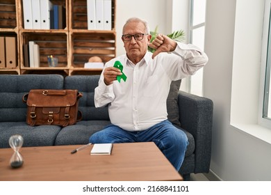 Senior Therapist With Grey Hair Holding Support Green Ribbon For Mental Health Awareness With Angry Face, Negative Sign Showing Dislike With Thumbs Down, Rejection Concept 