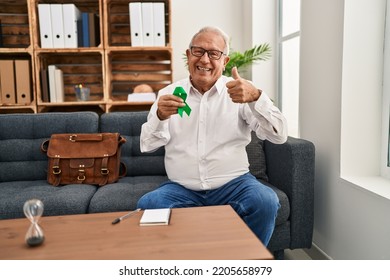 Senior Therapist With Grey Hair Holding Support Green Ribbon For Mental Health Awareness Smiling Happy And Positive, Thumb Up Doing Excellent And Approval Sign 