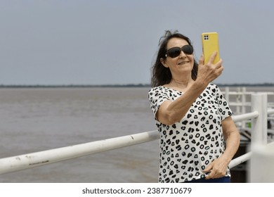 Senior tourist woman takes selfies on the river coast. - Powered by Shutterstock