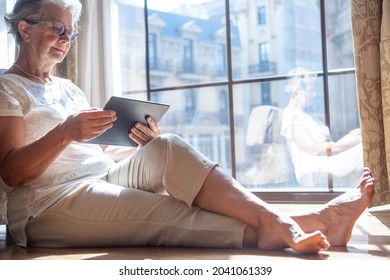 Senior Traveler Woman In Hotel Room Sitting On The Floor Consulting Her Digital Tablet To Organize A City Tour