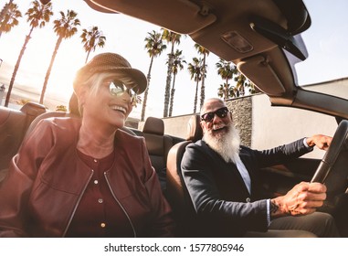 Senior trendy couple inside a convertible car on holiday time - Mature rich people having fun doing a road trip during vacation - Travel, fashion and joyful elderly concept - Main focus on man face
