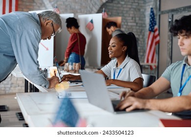 Senior US citizen signing up for voting with help of African American female volunteer at polling place. - Powered by Shutterstock