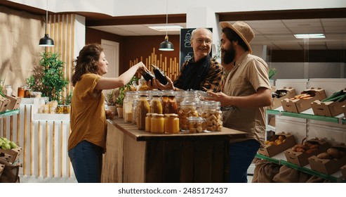 Senior vendor assisting clients in eco friendly shop with ethical sourced chemicals free food items. Couple in local store chatting with trader about pantry staples bulk products, zoom out - Powered by Shutterstock