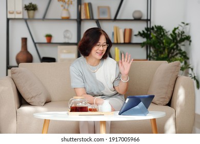 Senior Vietnamese Woman Drinking Tea And Video Calling Her Friends Or Relatives Via Application On Tablet Computer