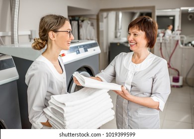 Senior Washwoman Making Up Clean Towels With Young Assistant In The Hotel Laundry