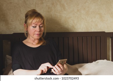 senior well-groomed middle-aged woman 40s 50s holding mobile phone lying bed at home. Portrait  attractive mature woman using texting reading message smartphone sitting sofa  - Powered by Shutterstock