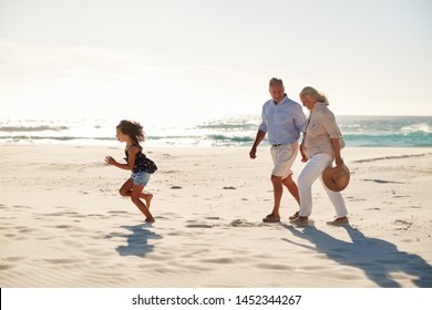 Senior White Couple And Their Granddaughter Walking On A Sunny Beach, Side View