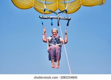 Senior white woman with gray hair is fearless and fun parasailing. Extreme sports concept. Close up