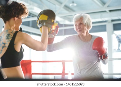 Senior white-haired woman in activewear and boxing gloves fighting with rival while training before competition - Powered by Shutterstock