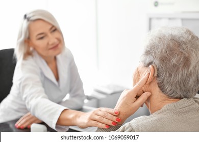 Senior Woman Adjusting Hearing Aid In Doctor's Office