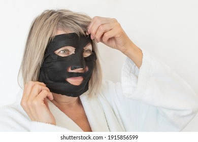 Senior Woman Applies Black Cosmetic Mask To Her Face. Anti Age Concept. Mature Woman Face After Spa Treatment. Beauty Spa Treatment. Plastic Surgery Clinic, Cosmetology, New Senior