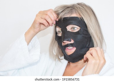 Senior Woman Applies Black Cosmetic Mask To Her Face. Anti Age Concept. Mature Woman Face After Spa Treatment. Beauty Spa Treatment. Plastic Surgery Clinic, Cosmetology, New Senior