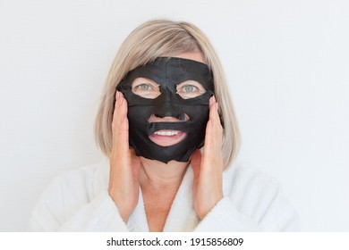 Senior Woman Applies Black Cosmetic Mask To Her Face. Anti Age Concept. Mature Woman Face After Spa Treatment. Beauty Spa Treatment. Plastic Surgery Clinic, Cosmetology, New Senior