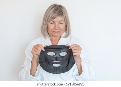 Senior Woman Applies Black Cosmetic Mask To Her Face. Anti Age Concept. Mature Woman Face After Spa Treatment. Beauty Spa Treatment. Plastic Surgery Clinic, Cosmetology, New Senior