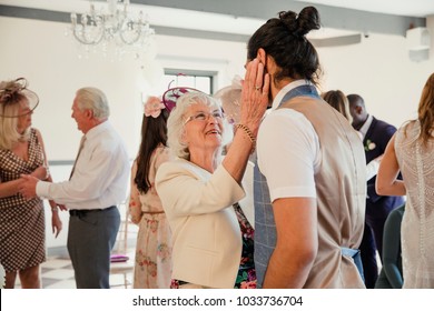 Senior Woman Is Appreciating Her Grandson On His Wedding Day. She Is Dancing And Talking To Him With Her Hands On His Face. 