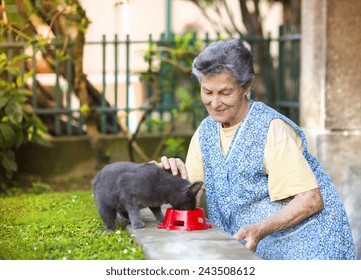 Senior woman in apron with her gray cat outside her house.