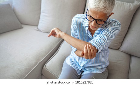 Senior woman with arm pain.Old female massaging painful hand indoors. Old woman hand holding her elbow suffering from elbow pain. Senior woman suffering from pain in hand at home. Old age, health 
