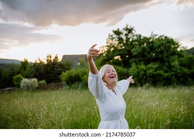 Senior Woman With Arms Outstretched And Face Up At Park On Summer Day, Mental Health Concept.