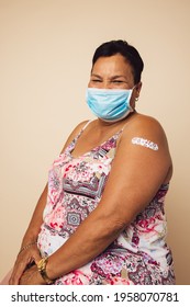 Senior Woman With Bandage On Her Arm After Getting Vaccine. Happy Female Wearing Protective Face Mask Looking At Camera After Receiving Corona Virus Vaccination.