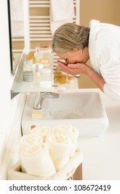 Senior Woman In Bathroom Washing Her Face At Wash Basin