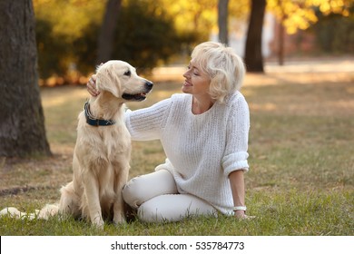 Senior Woman And Big Dog Sitting On Grass In Park