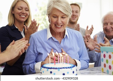 Senior Woman Blows Out Birthday Cake Candles At Family Party