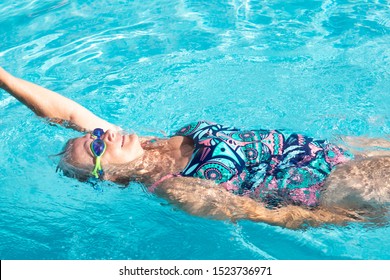 A senior woman with blue  swimming pool goggles swims in the transparent  water of the swimming pool. Healthy activity for pensioner. Lifestyles