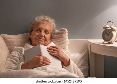 Senior Woman With Book Sleeping In Bed At Night