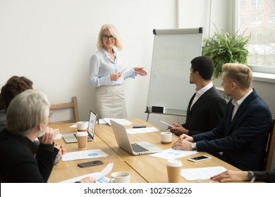 Senior Woman Boss Leading Corporate Team Meeting Presenting Team Goals, Smiling Aged Businesswoman Company Leader Or Business Teacher Giving Presentation Coaching Diverse Employees Group In Boardroom