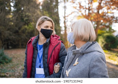 Senior Woman And Caregiver Outdoors On A Walk In Park, Coronavirus Concept.