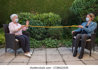 Senior Woman And Caregiver With Protective Masks Measuring Safety Distance