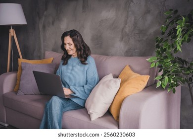 Senior woman in casual sweater enjoying leisure time on laptop at home indoors - Powered by Shutterstock