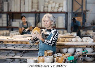 Senior woman ceramist arranging new bowls in workshop. Photo of skillful female handicraft worker. - Powered by Shutterstock