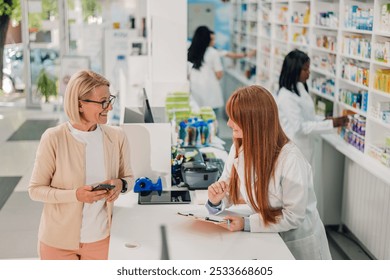 Senior woman chats with a pharmacist at a pharmacy counter, surrounded by pills and drugs. The pharmacist provides advice as they discuss healthcare options - Powered by Shutterstock