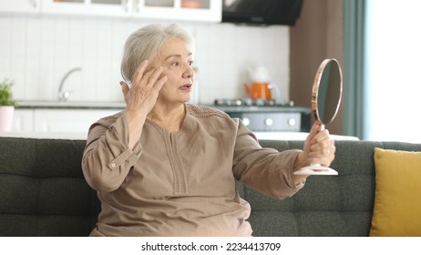 Senior woman checking her skin and hair while looking in the mirror. Happy smiling senior woman pampering herself,enjoying healthy skin care, aging beauty,skincare treatment cosmetic products concept. - Powered by Shutterstock