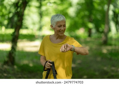 Senior woman checks smartwatch after nordic walking in the park for fitness tracking. - Powered by Shutterstock