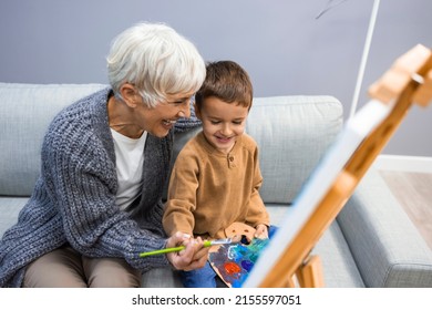 Senior woman and child painting canvas  Grandmother spending happy time and grandson  Small boy listening to his grandmother who is teaching him to paint canvas at home 