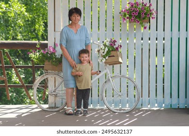 Senior woman and child standing beside a decorative bicycle with flowers. Kid aged three year (three year old boy) - Powered by Shutterstock