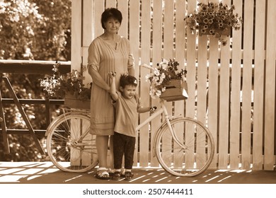 Senior woman and child standing beside a decorative bicycle with flowers. Outdoor portrait for design and print. Kid aged three year (three year old boy) - Powered by Shutterstock