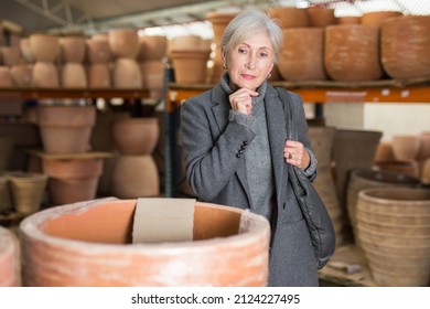 Senior Woman Choosing Earthenware Pot In Crockery Store.