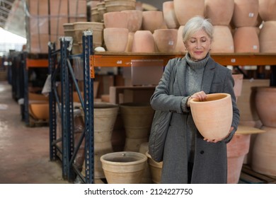 Senior Woman Choosing Earthenware Pot In Crockery Store.